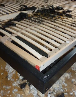 Brandschaden an einem Bett durch eine verbrannte Heizdecke mit starken Rußablagerungen und beschädigter Matratze.